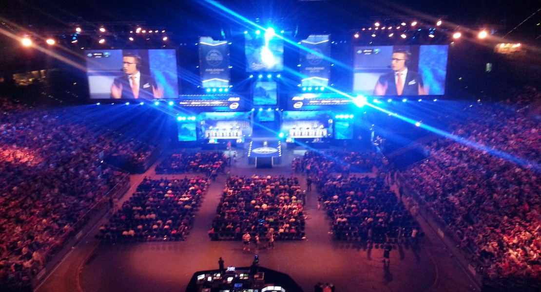A bird's eye view of the LANXESS Arena. Production team at the back of the ground floor seating area. Casters on the screens doing pre-match discussions.