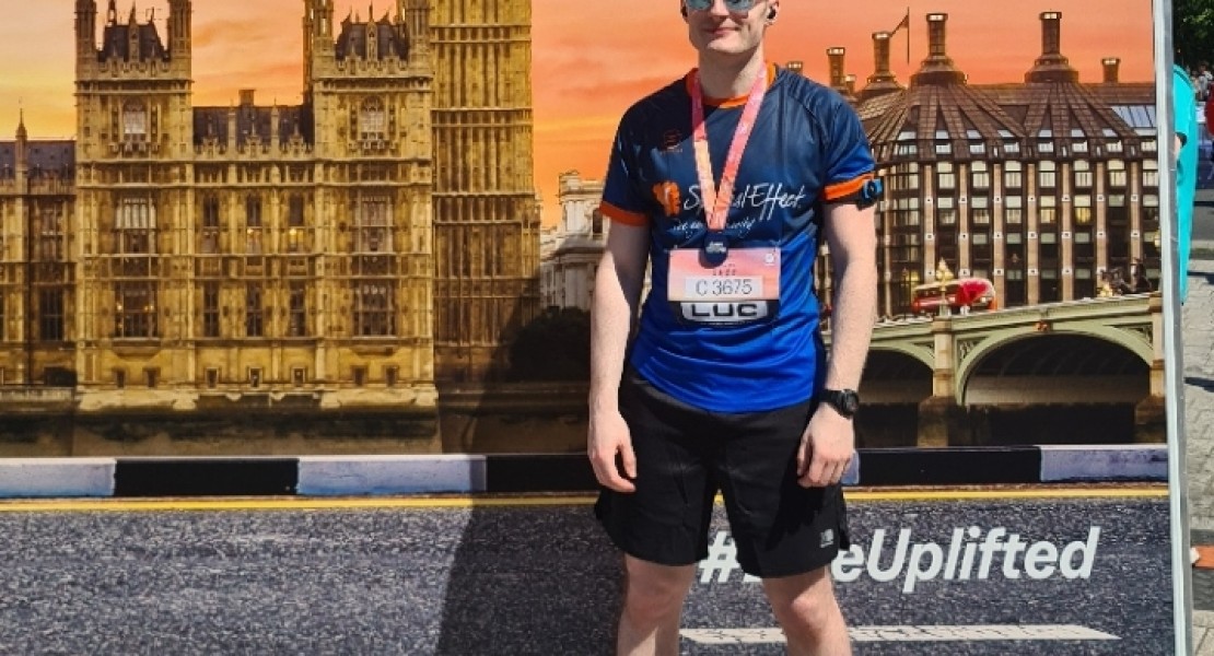 A picture of myself (Luc Shelton) posing with my medal after running the ASICS London 10K. I'm standing in front of a photo backdrop.